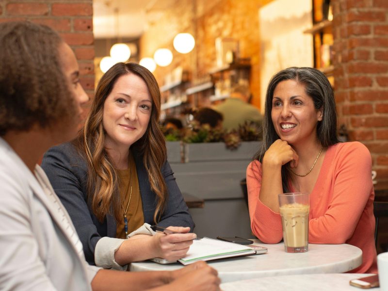 A photo of three Women sat taking notes and chatting in a restaurant or bar setting.